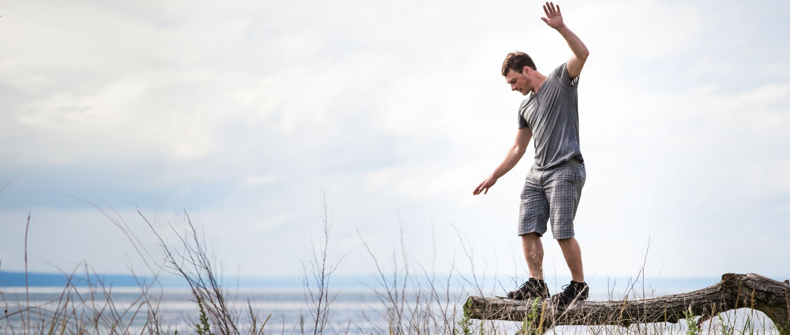 Junger Mann balanciert auf einem Baumstamm am Meer